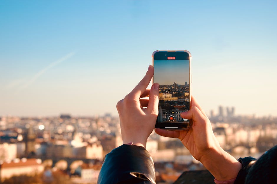 Hands holding a smartphone taking a photo of a city skyline during sunset, reflecting modern travel and technology.